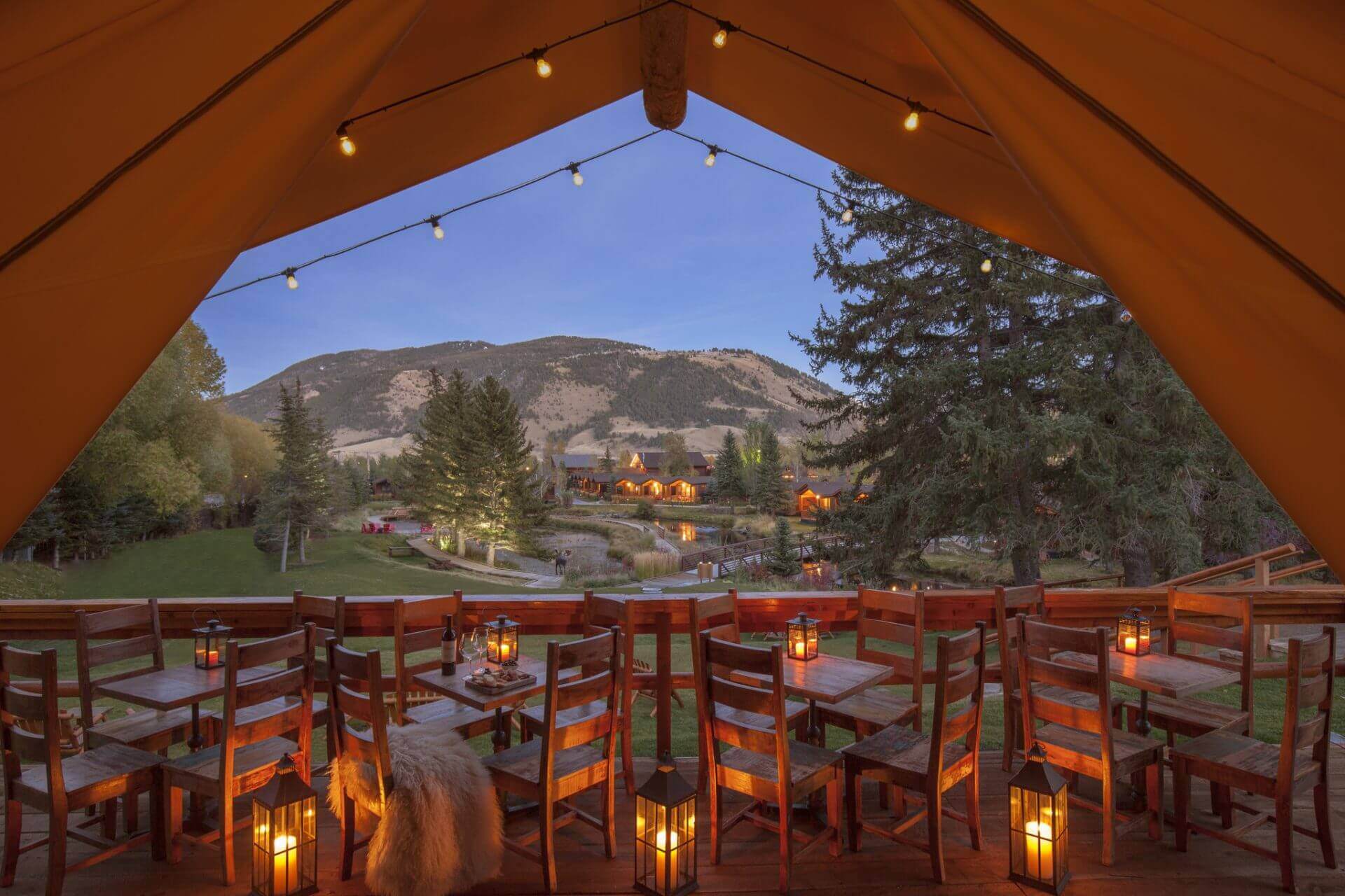 wooden tables under a canvas tent outside with lantern lights on them overlooking Rustic Inn