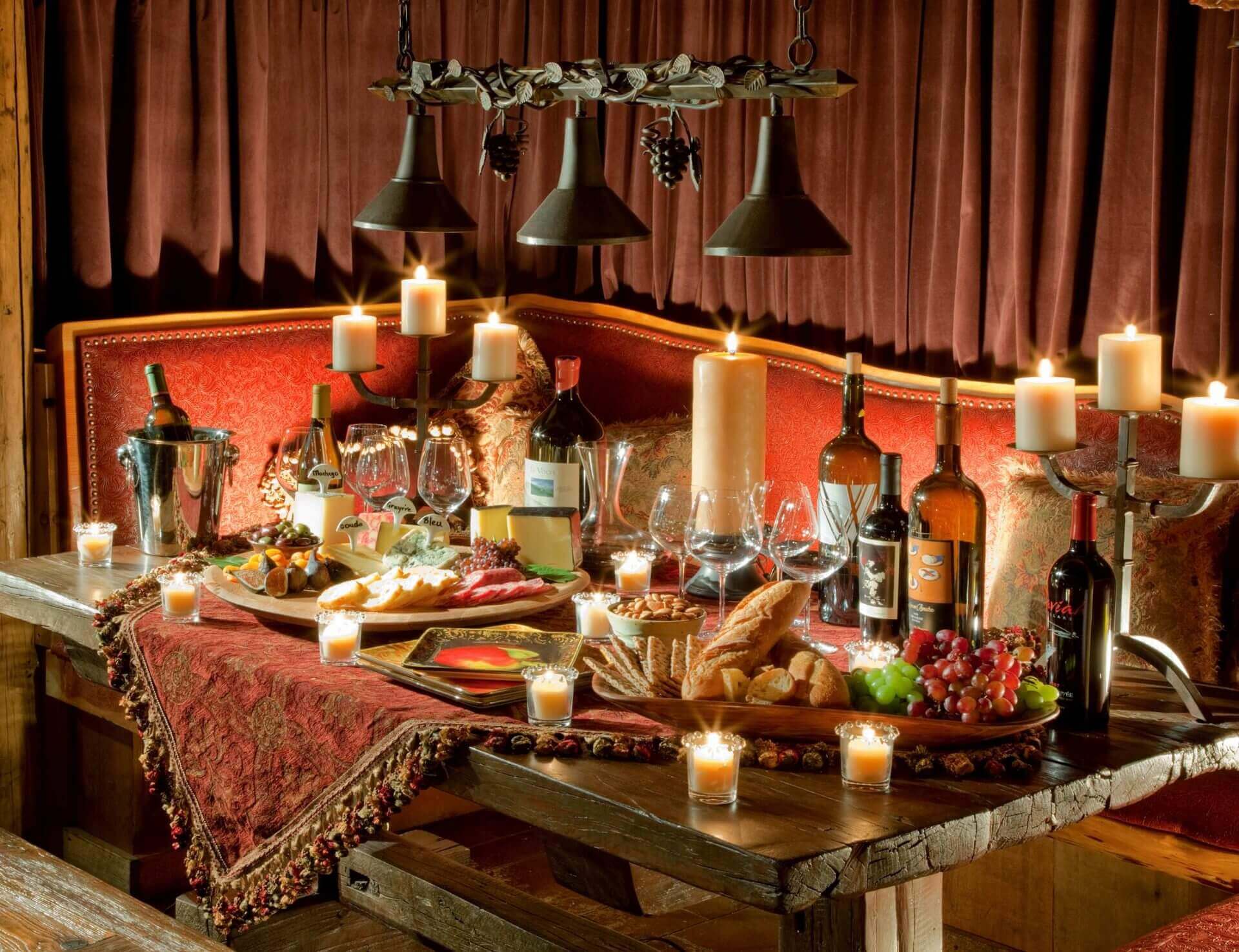 dining table with several bottles of wine, candles and fruit and cheese platters