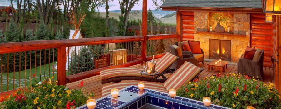 outdoor hot tub lined with candles next to a deck with a fireplace