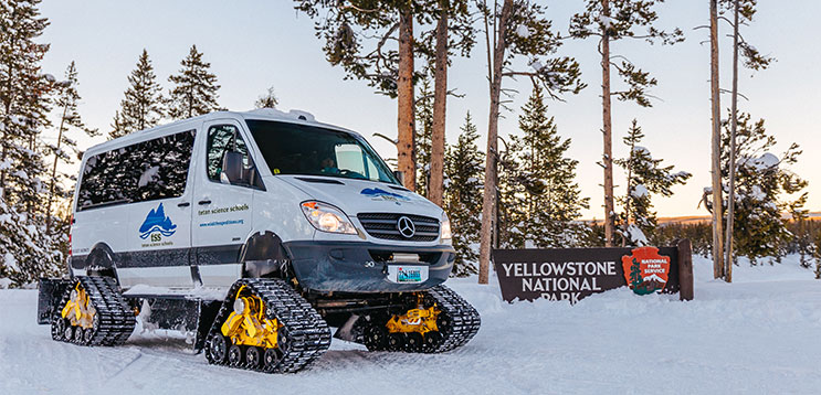 snowcoach van parked by Yellowstone sign in winter