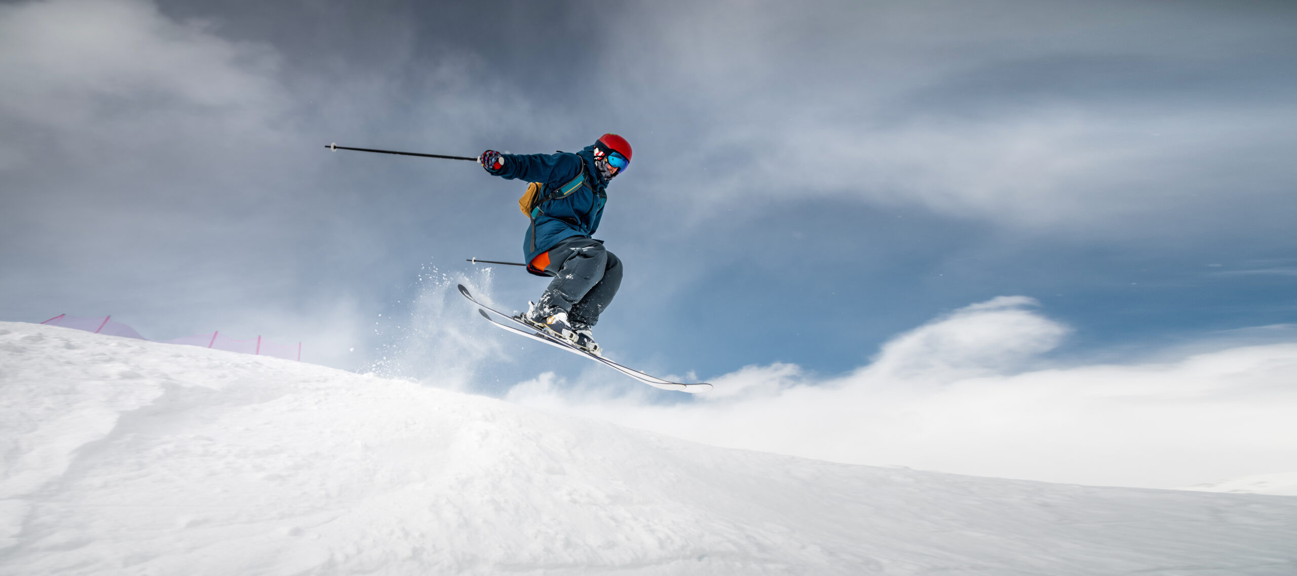 A sportsman skier in ski equipment jumps down a steep snowy slope of a mountain.